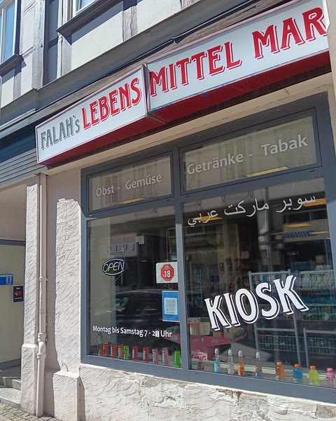 Die Ladenfront mit dem rot-weißen Schild Falah's Lebensmittel Markt und der Aufschrift KIOSK auf der Scheibe